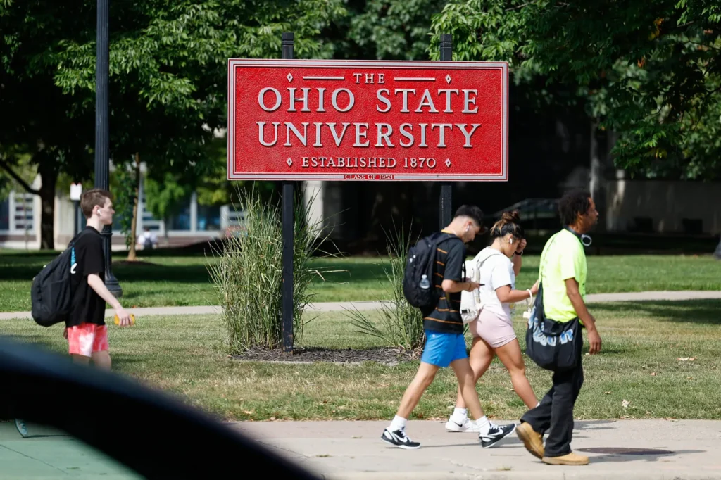 Several students are walking across the campus in front of a sign that says "Ohio State University"
